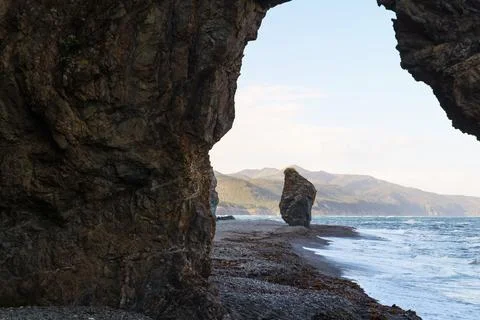 View of the beach by the ocean and cliffs through a stone arch Stock Photos