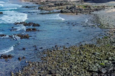 View of beach waves breaking on dark rocks during low tide. Paradise beach... 库存照片