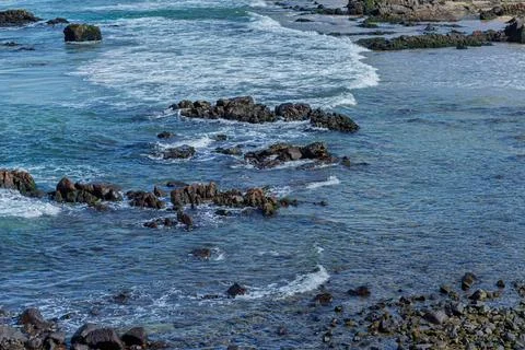 View of beach waves breaking on dark rocks during low tide. Paradise beach... Photos