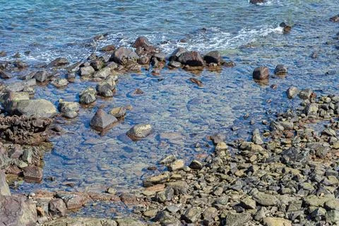 View of beach waves breaking on dark rocks during low tide. Paradise beach... Stock Photos