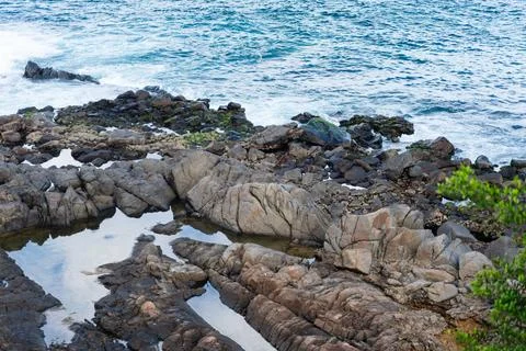 View of beach waves breaking on dark rocks during low tide. Paradise beach... Photos