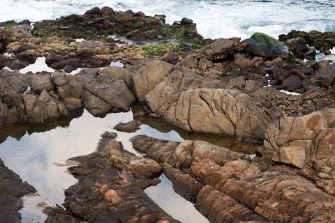 View of beach waves breaking on dark rocks during low tide. Paradise beach... Photos