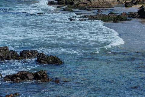 View of beach waves breaking on dark rocks during low tide. Paradise beach... Photos