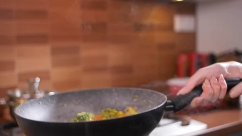 View of beautiful female hands throwing up freshly-cooked vegetables in the pan Stock Footage 107437930