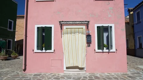 View on beautiful pink house with flowerpots and curtain on door in Burano Stock Footage