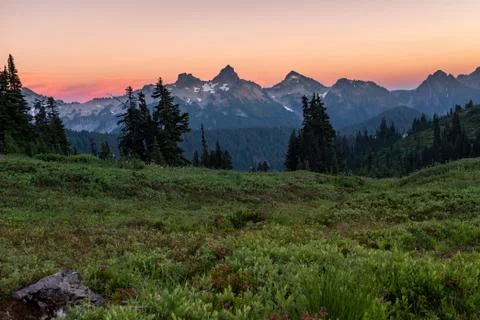 A view of a beautiful sunset over a range of mountains from across a meadow w Stock Photos