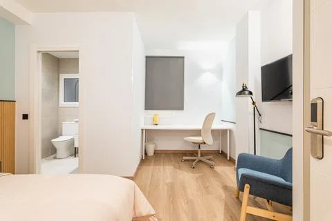 View of bedroom with large bed, work area with white wooden table and Stock-Fotos
