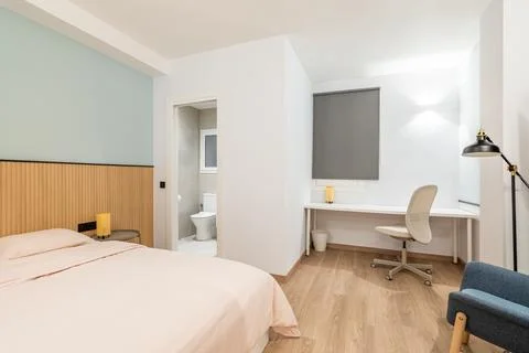 View of bedroom with large bed, work area with white wooden table and Stock Photos