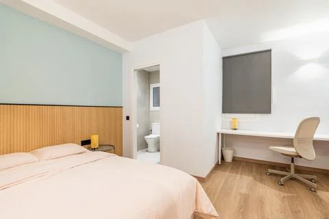 View of bedroom with large bed, work area with white wooden table and Stock Photos