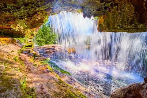 View behind and inside of waterfall cave of orange and lichen growth with sun Stock Photos