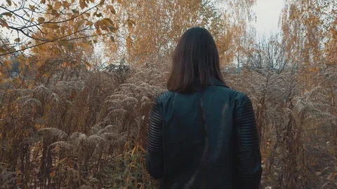 View from behind female in a leather jacket walks through the field of  reeds Video stock 128952098