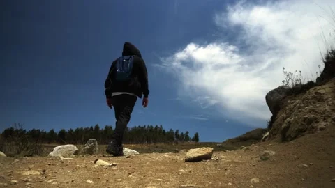 View from behind of a man with hood and backpack walking on a mountain trek 스톡 동영상 164596648