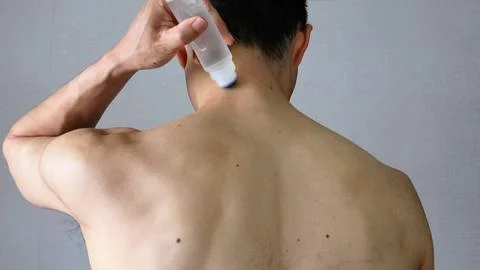 A view from behind of a person applying a medicated patch to their body. Stock Photos