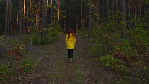 View from behind of red haired woman in yellow raincoat walking through forest Stock Footage 135533557