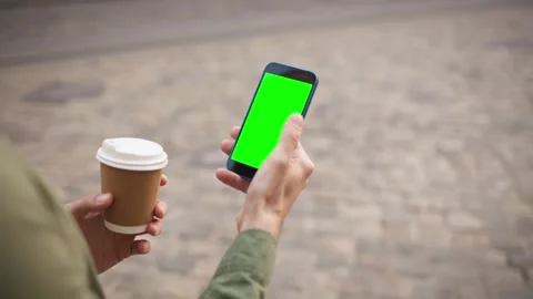 View from behind shoulder of someone using smartphone with green screen. Holding Stock Footage 275975183