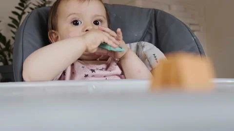 View from behind table of a baby sitting on a high-chair and scratching his Stock Footage 170468733