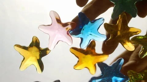 View from below as a hand pours artificial colored starfish. Background for the Stock Footage 122594055