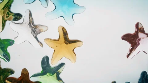 View from below as a hand pours artificial colored starfish. Background for the Stock Footage 122606401