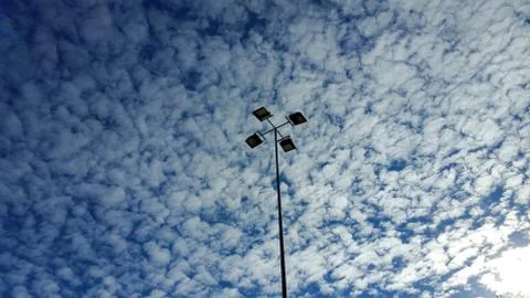 View from below on a lamp post with four lamps, against a cloudy sky Stock Photos