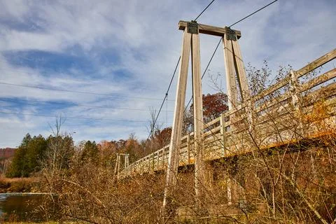 View below large suspension bridge going over river near fall fields and forests Stock Photos