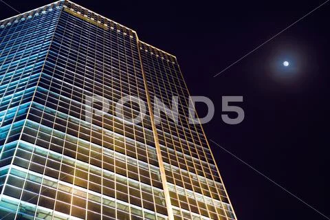 View from below of office building at night with full moon in the sky Stock Photos