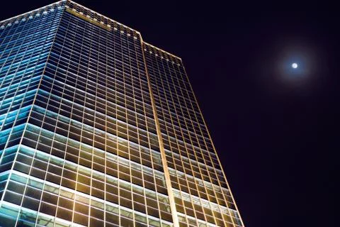 View from below of office building at night with full moon in the sky Stock Photos