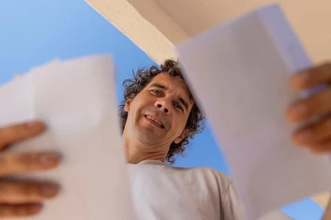 A view from below of a young man reading a letter while standing near a mai.. Stock Photos