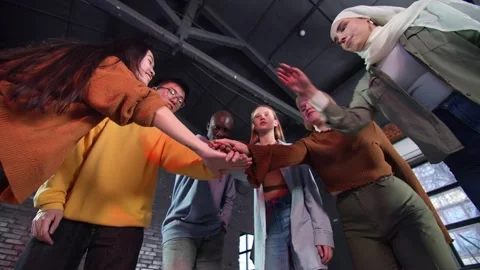 A view from below of young motley people holding hands, demonstrating unity team Stock Footage 233219024