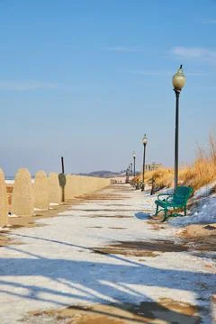 View of bench and light posts lining walkway in winter 스톡 사진