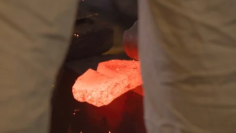 View between legs of a Master black smith pounding red hot ingot Stock-Footage 125434564