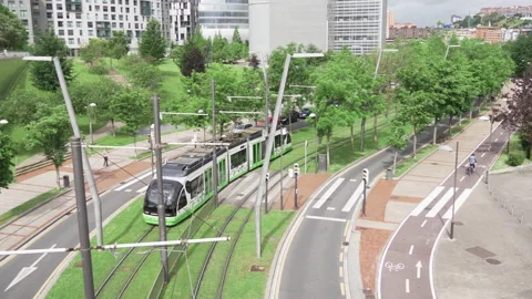 View of the Bilbao tram as it passes through gardens while a bicycle passes Stock Footage 160410877
