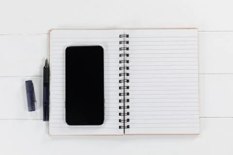 View of a black smartphone, a notebook and a black pen on plain white background Stock Photos