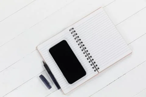 View of a black smartphone, a notebook and a black pen on plain white background Stock Photos
