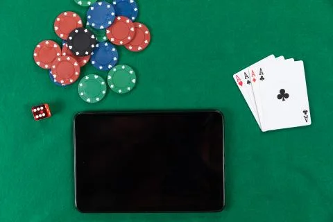 View of a black tablet, playing cards, a red dice and colorful tokens on plain Stock Photos