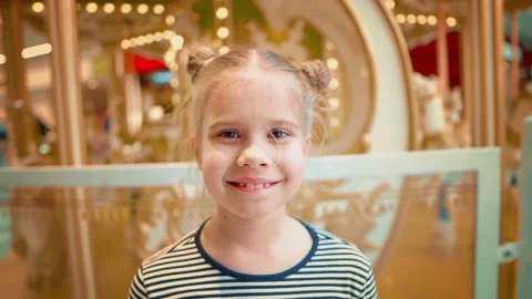 View of blond girl looking at camera against the background of glowing carousel Stock Footage 157319987
