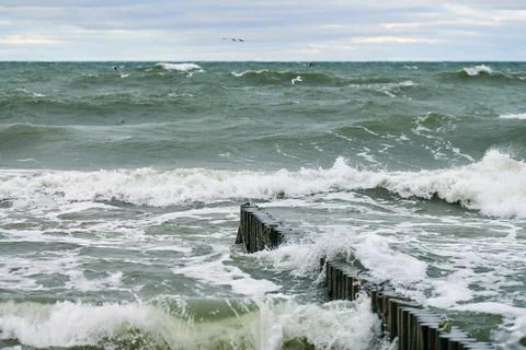 View of blue sea with foaming waves and wooden breakwaters Stock Photos
