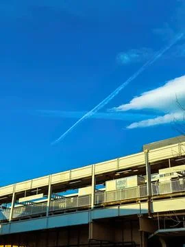 View of a blue sky with clouds and a diagonal jet trail above a highway Stock Photos