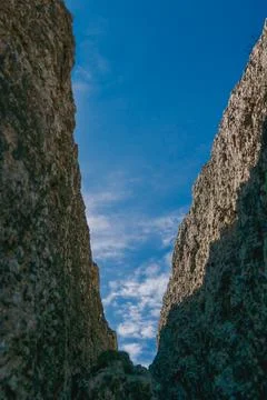 View of blue sky framed between two tall rocky cliffs with textured stone w.. Stock Photos