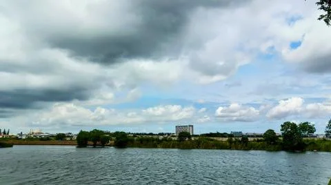 View of blue sky with thick clouds on the edge of a lake in an urban park. Stock Photos