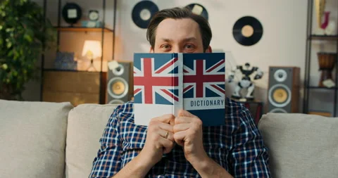 View of a book from English held by a man covering face with it. The man slowly Stock Footage 200830225