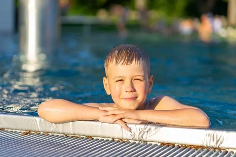 View of a boy holding onto the side of a pool, a boy swimming in an outdoor.. Stock-Fotos