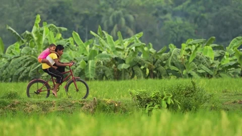 View of a boy riding a bicycle with a child on his back, Bangladesh. Stock Footage 335600024