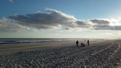 View into a bright sun along a sandy beach with tourists and vehicle tracks Video stock 152881901