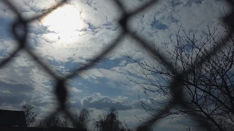 View of bright sun through a chain-link fence against blue sky with white c.. Vídeos de archivo 333792907