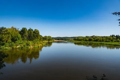 A view of the Bug River with its banks reflected in the water during the summ Stock-Fotos