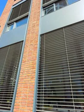View of a building with a brick wall and large windows. Horizontal blinds cov Stock Photos