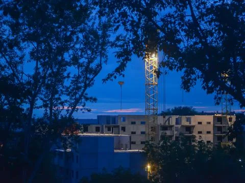 A view of the building under construction and the crane in the twilight through Stock Photos
