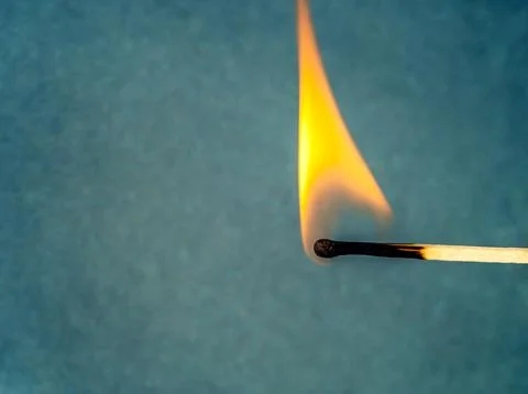 View of burning match with flame on blue blurred background. Close-up. Stock Photos