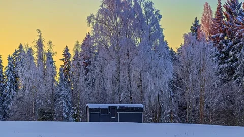 View of a cabin in a snowy forest at twilight, Latvia. Видео 340639841