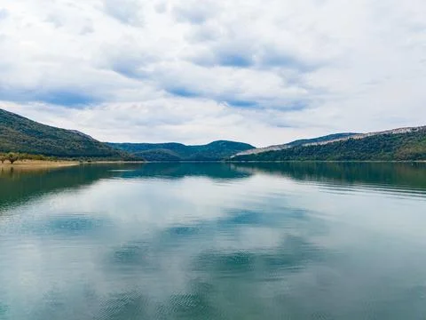View of a calm lake surrounded by mountains on a cloudy day with reflection.. Stock Photos